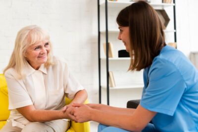 Old woman sitting on a yellow chair with a young female nurse in blue uniform nurse holding hands